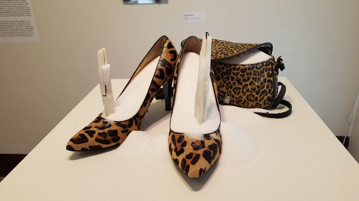 A pedestal with a pair of leopard-print high-heeled shoes and matching purse filled to overflowing with salt; in each shoe a used candle is placed upright.