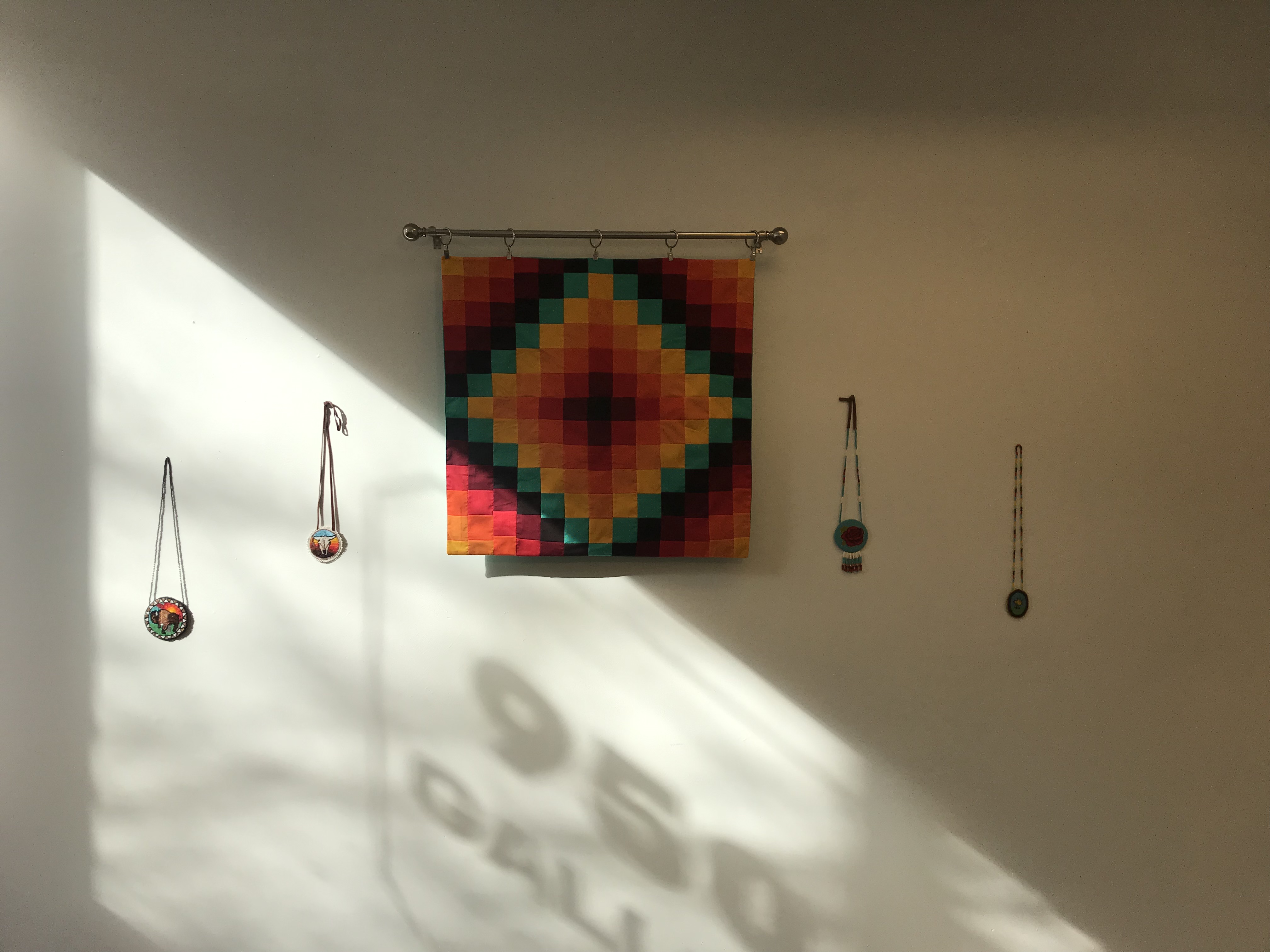 A colorful geometric fabric hanging and four beaded necklaces arranged on a wall.